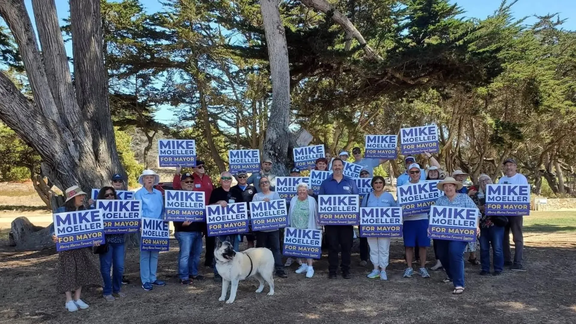 Supporters holding Mike Moeller for Mayor signs at a gathering under the cypress trees in Marina